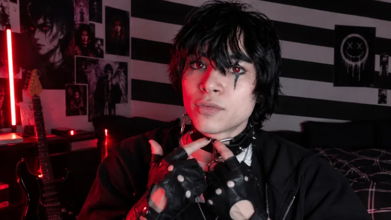 Corpse Husband seated at a microphone in a darkened home studio with his face hidden